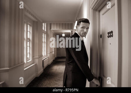 Good looking man in hotel corridor using key card to open room door Stock Photo