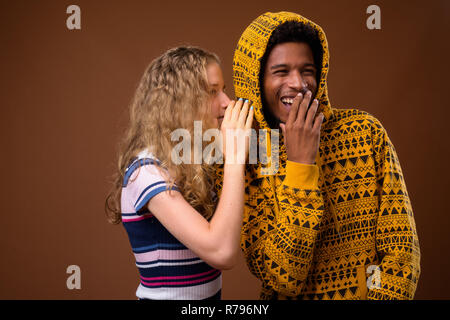 Teenager girl whispering to happy African man who is laughing Stock Photo