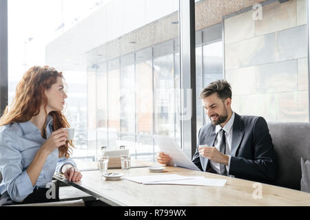 Businesspeople having coffee break at restaurant sitting drinking espresso man looking at documents joyful while woman looking at him thoughtful Stock Photo