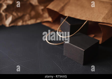 Two matte black carton gift boxes laying on a black painted scratched surface, craft paper bag blurred on background, home gift wrapping craft theme Stock Photo