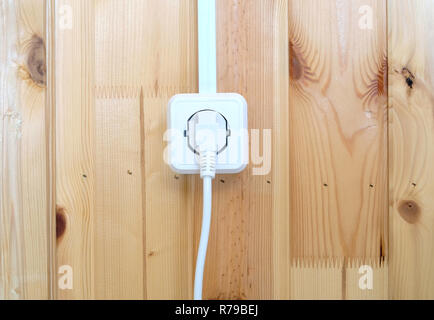 White electric plug in socket on wooden wall with vertical planks front view closeup Stock Photo