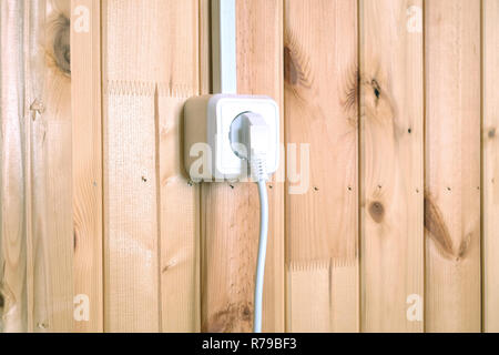 White electric plug in socket on wooden wall with vertical planks side view closeup Stock Photo