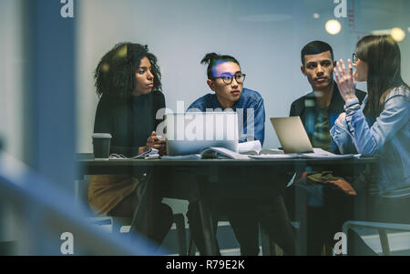 Woman talking with classmates while studying together around table. Young people sitting at the table working on an assignment. Stock Photo