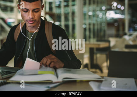Male student sitting at table reading books and preparing for exams. Young man reading book at university library. Stock Photo