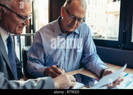 Two coworkers working on a project while at a cafe. Senior businessmen working together in a cafe, making notes. Stock Photo