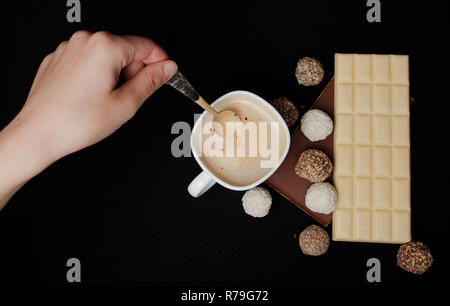 Woman adding sugar in coffee in cafe. Cofe, Stack of Black and White Chocolate isolated on black background, place for text. Stock Photo