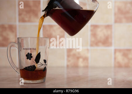 A glass kettle and a glass cup with tea on the table. From a transparent kettle pours pouring tea into a mug Stock Photo