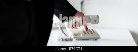 Wide view image of businessman in a suit holding white landline receiver dialing a telephone number. Stock Photo