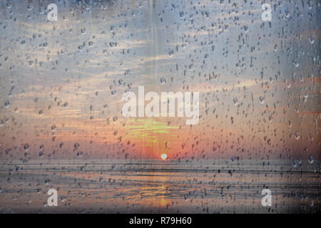 sun sets over the sea in holland seen through raindrops on window pane Stock Photo