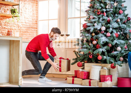 Man putting gifts under the Christmas tree preparing for a New Year holidays at home Stock Photo