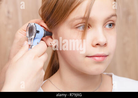 Female pediatrician examines elementary age girl's ear. Doctor using a otoscope or auriscope to check ear canal and eardrum membrane. Child ENT check  Stock Photo