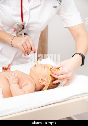 Close-up shot of pediatrician examines two months baby boy. Doctor using measurement tape checking baby head size Stock Photo