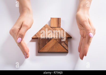 Woman Protecting House Made Of Wooden Tangram Puzzle Stock Photo