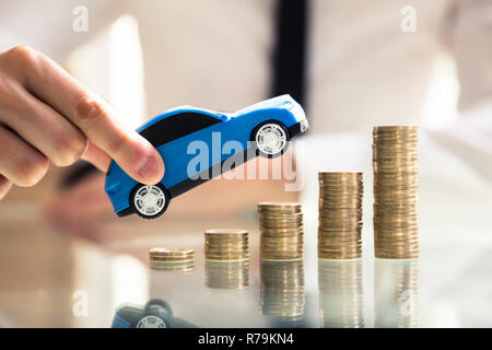 Person Holding Car Over Rising Stacked Coins Stock Photo
