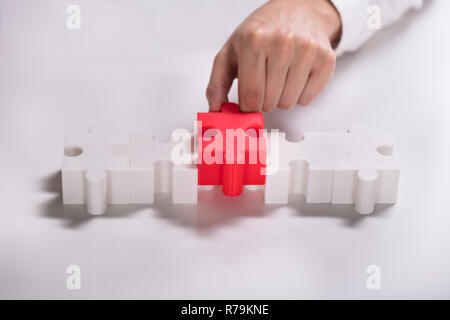 Person Placing Red Piece Between White Jigsaw Puzzles Stock Photo