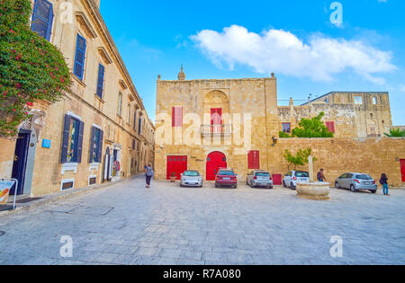 MDINA, MALTA - JUNE 14, 2018: The small St Agatha square with small stone fountain with a pillar and low edifices around, on June 14 in Mdina. Stock Photo