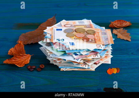 A lot of euro banknotes and coins with leaves and coffee beans on blue background. Stock Photo