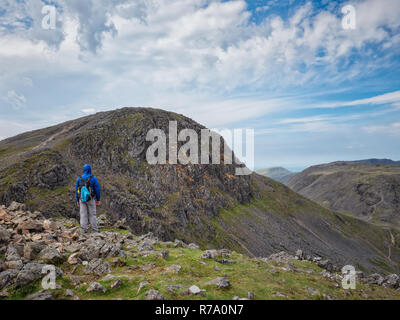 A walker looks ahead to the mountain summit of Great Gable from Windy Gap in the Lake District, Cumbria, England. Stock Photo
