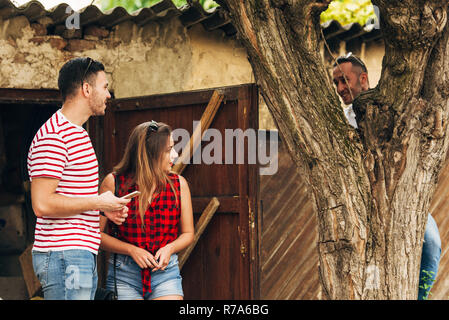 Carefree couple standing next to a tree, while his friends climbing on a tree Stock Photo