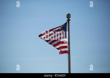 American flag waving vigorously in the wind against a blue sky Stock Photo