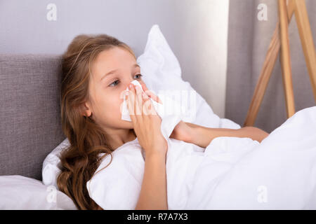 Girl Suffering From Cold Blowing Her Nose With Handkerchief On Bed Stock Photo