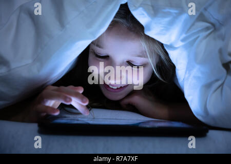 Close-up Of A Happy Girl Under White Blanket Using Digital Tablet Stock Photo