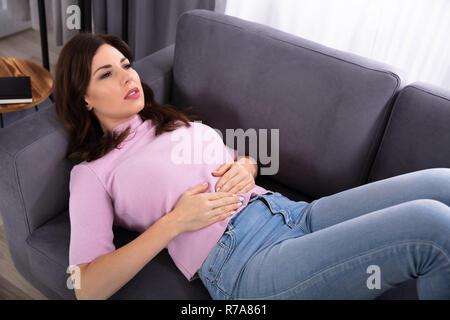 Young Woman Lying On Sofa Suffering From Stomachache At Home Stock Photo