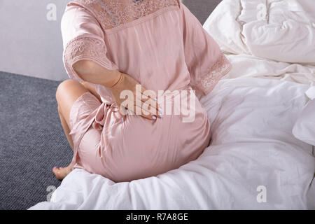 Rear View Of A Woman Sitting On Bed Suffering From Back Pain In Bedroom Stock Photo