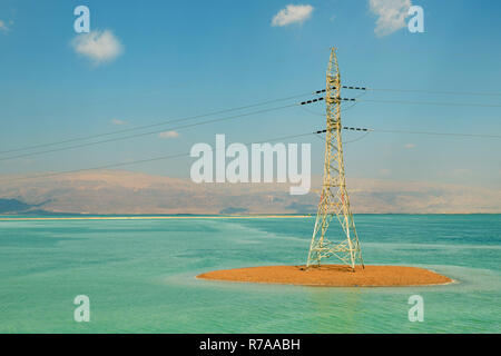 Electricity tower on a sandy embankment against a blue sky with clouds, a tower with wires against the backdrop of the mountains of Jordan in the Dead Stock Photo