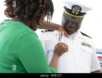 MANAMA, Bahrain (April 12, 2017) Lt. Cmdr. Roosevelt White's wife tacks the Command at Sea pin on White's uniform as he takes command during the Avenger-class mine countermeasures ship USS Gladiator's (MCM 11) change of command ceremony at Naval Support Activity Bahrain. Gladiator, part of U.S. Naval Force Central Command's Task Force (TF) 52, is one of four Avenger-class MCM ships home-ported in Manama. TF 52 provides command and control of all mine warfare in the U.S. 5th Fleet area of operations, which encompasses 2.5 million miles of water area including the Arabian Gulf, Gulf of Oman, Red Stock Photo