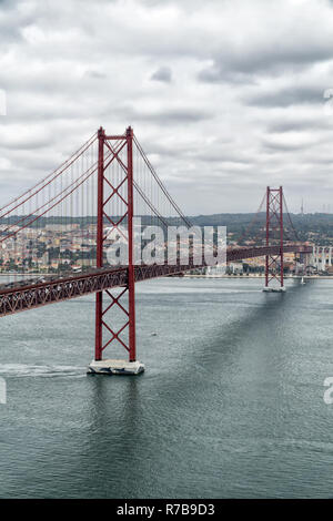 Famous 25th of April Bridge over Tagus River in Lisbon, Portugal on a cloudy day. View from the left (south) bank of the Tagus river. Stock Photo