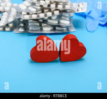 two red wooden hearts on a blue background, behind a stack of pills Stock Photo