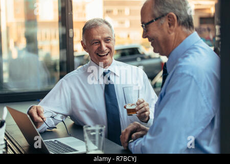 Two senior business professionals having a casual discussing at cafe. Senior businessmen laughing while sitting at cafe with laptop. Stock Photo