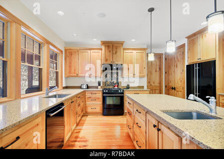 Beautiful kitchen with light wood cabinets, granite counter tops and black appliances. Stock Photo