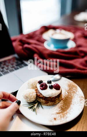 Top view of designers place. Womens hand keep spoon. Freelance working space. Notebook with mobile phone, cup of coffee and dessert on wooden table. Stock Photo