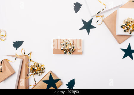 One gift among flat lay frame of Christmas decorations of boxes, bows and ribbons of black and gold colors on white table, top view. Stock Photo