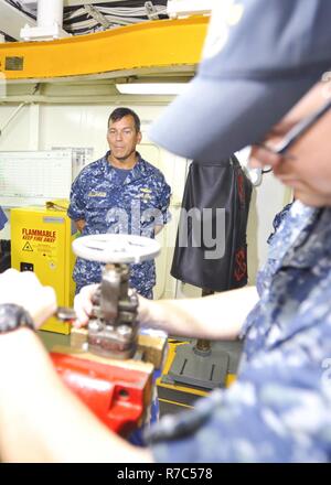 (POLARIS POINT, Guam) May 16, 2017 -- Rear Adm. Stephen Williamson, Director of Fleet Maintenance, U.S. Pacific Fleet, watches Machinist's Mate 3rd Class Steven Cool perform preventative maintenance on a valve during a tour aboard submarine tender USS Emory S. Land (AS 39), May 16. Williamson toured the ship and other repair facilities in Guam to assess current operations and capabilities. Land and USS Frank Cable (AS 40), the U.S. Navy’s only two submarine tenders, are both homeported in Apra Harbor, Guam, and provide maintenance, hotel services, and logistical support to submarines and surfa Stock Photo