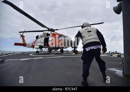 GULF OF ALASKA - A Chief Boatswain's Mate assigned to Arleigh Burke-class guided missile destroyer USS O'Kane (DDG 77) observes a U.S. Coast Guard MH-60T Jayhawk helicopter assigned to Air Station Kodiak, Alaska, landing during flight deck operations in the Gulf of Alaska. Northern Edge 2017 is Alaska's premiere joint-training exercise designed to practice operations, techniques, and procedures as well as enhance interoperability among the services. Thousands of participants from all the services; Sailors, Soldiers, Airmen, Marines, and Coast Guard personnel from active duty, Reserve and Natio Stock Photo