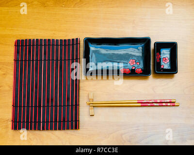 view from top flat lay of empty sushi set utensil tableware on wooden desk. stylish dishes, bamboo chopsticks and black red mat Stock Photo