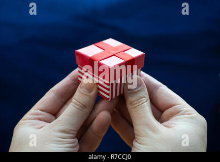 close-up two hands holding small red stripe gift box with blue background. nice color contrast Stock Photo