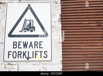 A warn and faded forklift warning sign on a wall with peeling paint beside a rusty roller shutter door Stock Photo