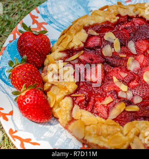 Homemade strawberry pie (galette) with almonds served on a ceramic plate decorated with fresh strawberries. Concept of homemade food and summer. Stock Photo