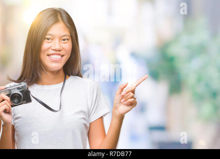 Young asian woman holding vintagera photo camera over isolated background very happy pointing with hand and finger to the side Stock Photo