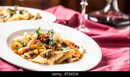 Idalian pasta pappardelle with beef ragout on white plate and red wine. Stock Photo