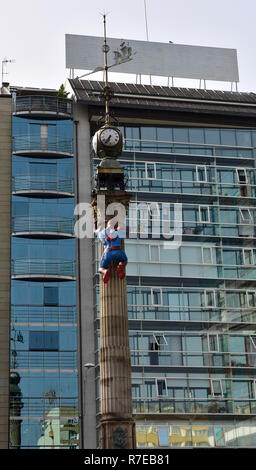 La Coruna Summer Comic Con, 2018. Spider-Man climbing an obelisk with wind vane and clock. Buildings with mirror windows. Spain. Stock Photo