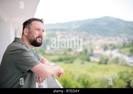 Portrait of successful happy young hipster man standing on a modern balcony overlooking the city in the background Stock Photo