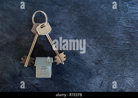 A bunch of keys lie on a vintage dark background along with an imitation of the house in the form of a metal layout. The concept of the offer of sale  Stock Photo