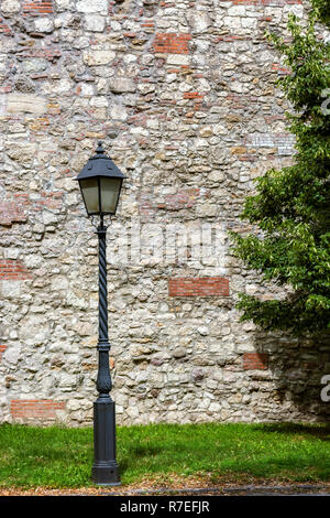 Street light on the pole on the background of old stone walls interspersed with red brick. Stock Photo