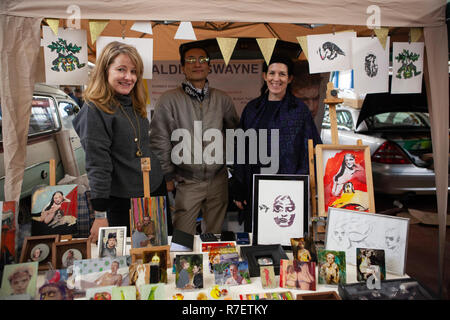 London, UK. 9th December 2018. The Art Car Boot Fair Christmas Wrap in Vauxhall allowed the public to buy art direct from artists. Artist Geraldine Swayne (left) and assistants at her stall. Credit: Anna Watson/Alamy Live News