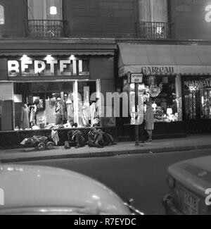 Three homeless people beg in front of a high class fashion store while a mother with her child looks at the items in the shop window of the neighboring shop in Paris, France, in November 1970. Photo. Wilfried Glienke | usage worldwide Stock Photo